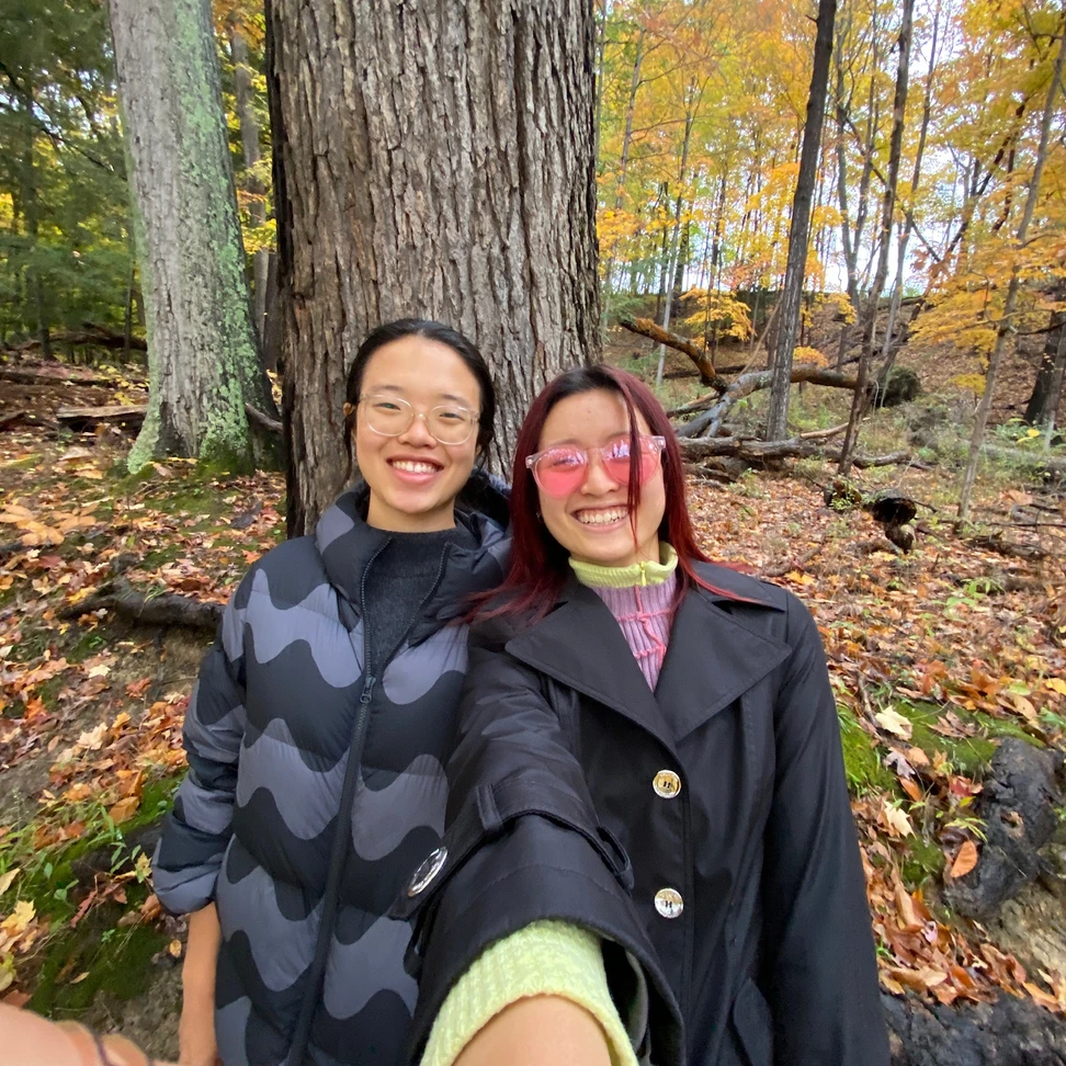 Two people standing amidst fall foliage and smiling.