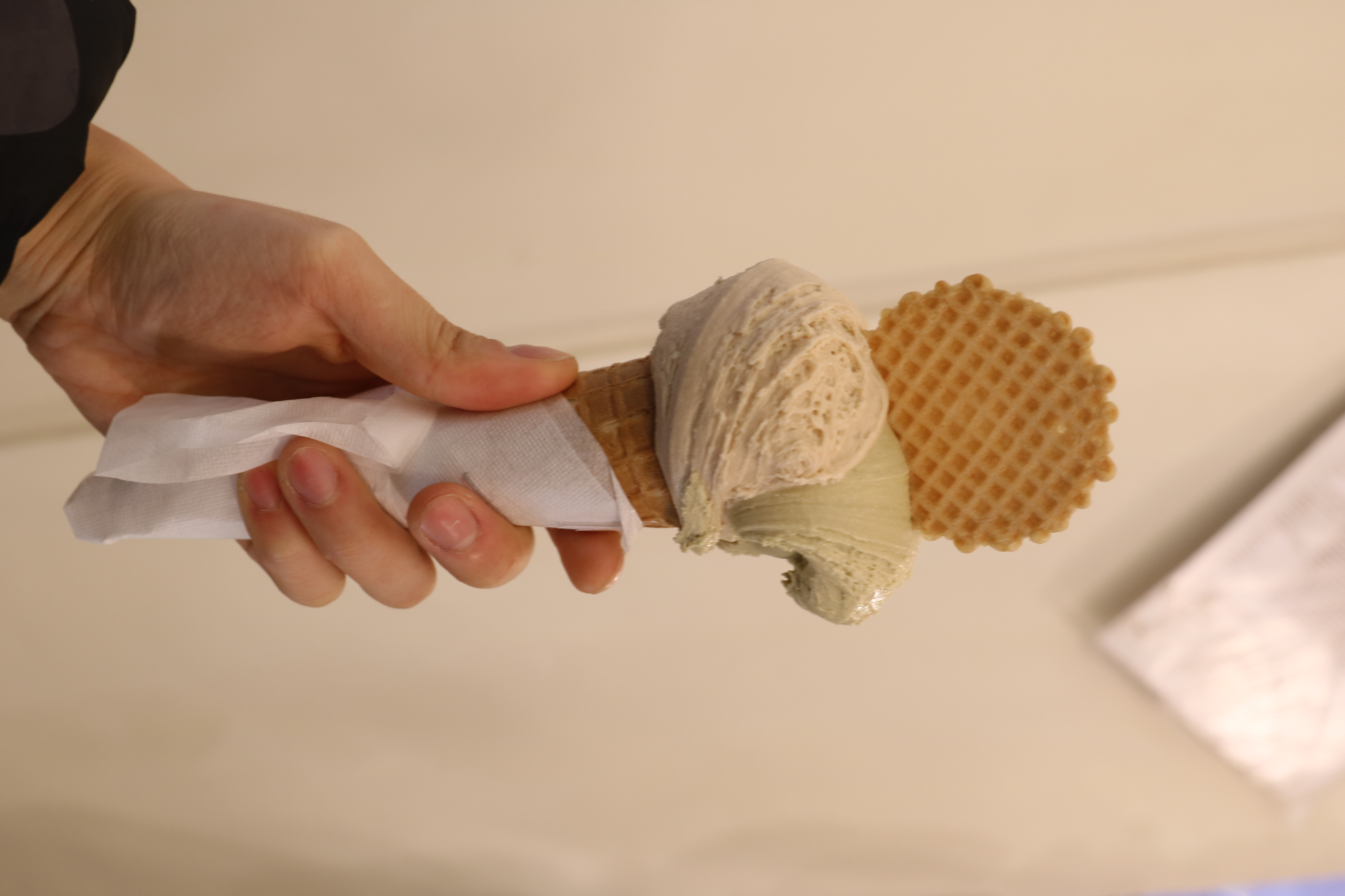 Hand holding gelato with hazelnut and pistachio ice cream.